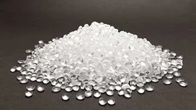 Clear plastic pellets piled on a dark surface.