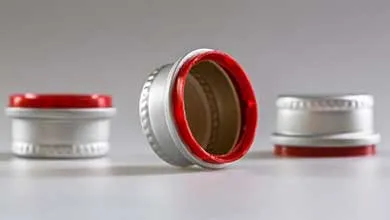 A silver screw cap with a red inner lining, lying on its side. Two similar caps are blurred in the background.